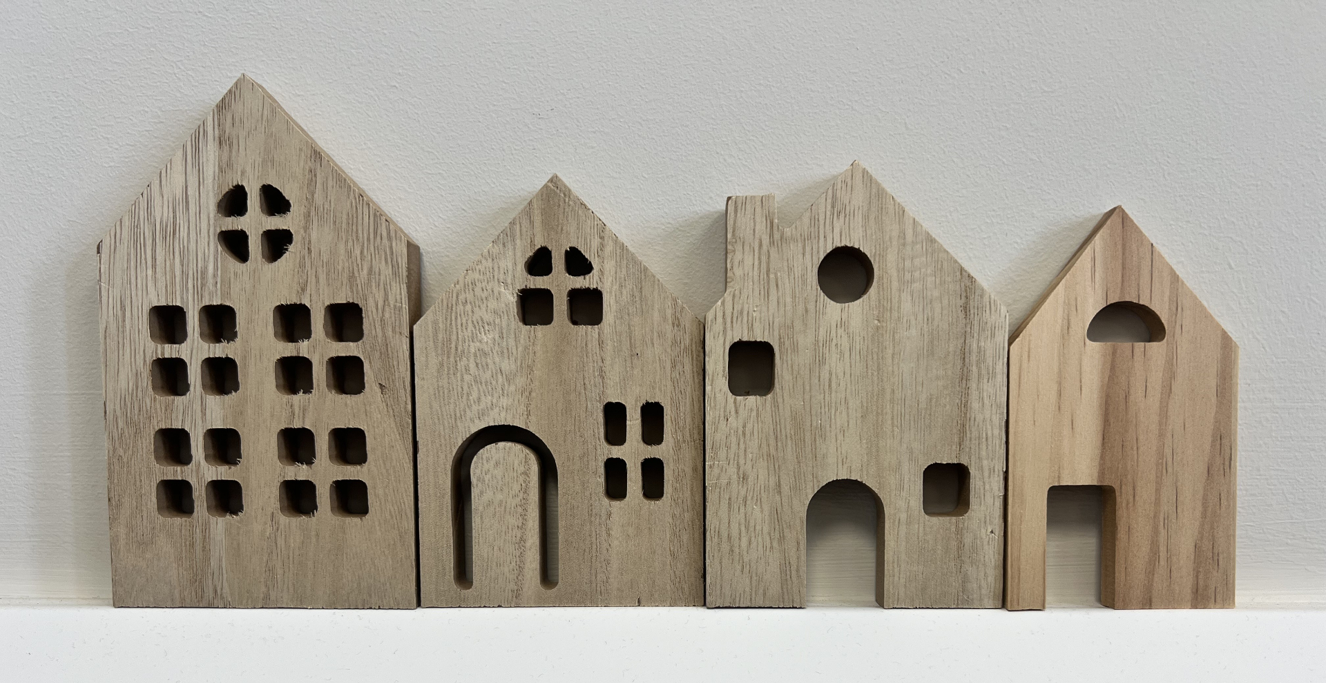 Four handcrafted wooden house sculptures with cut-out windows and doors, arranged in a row against a white wall