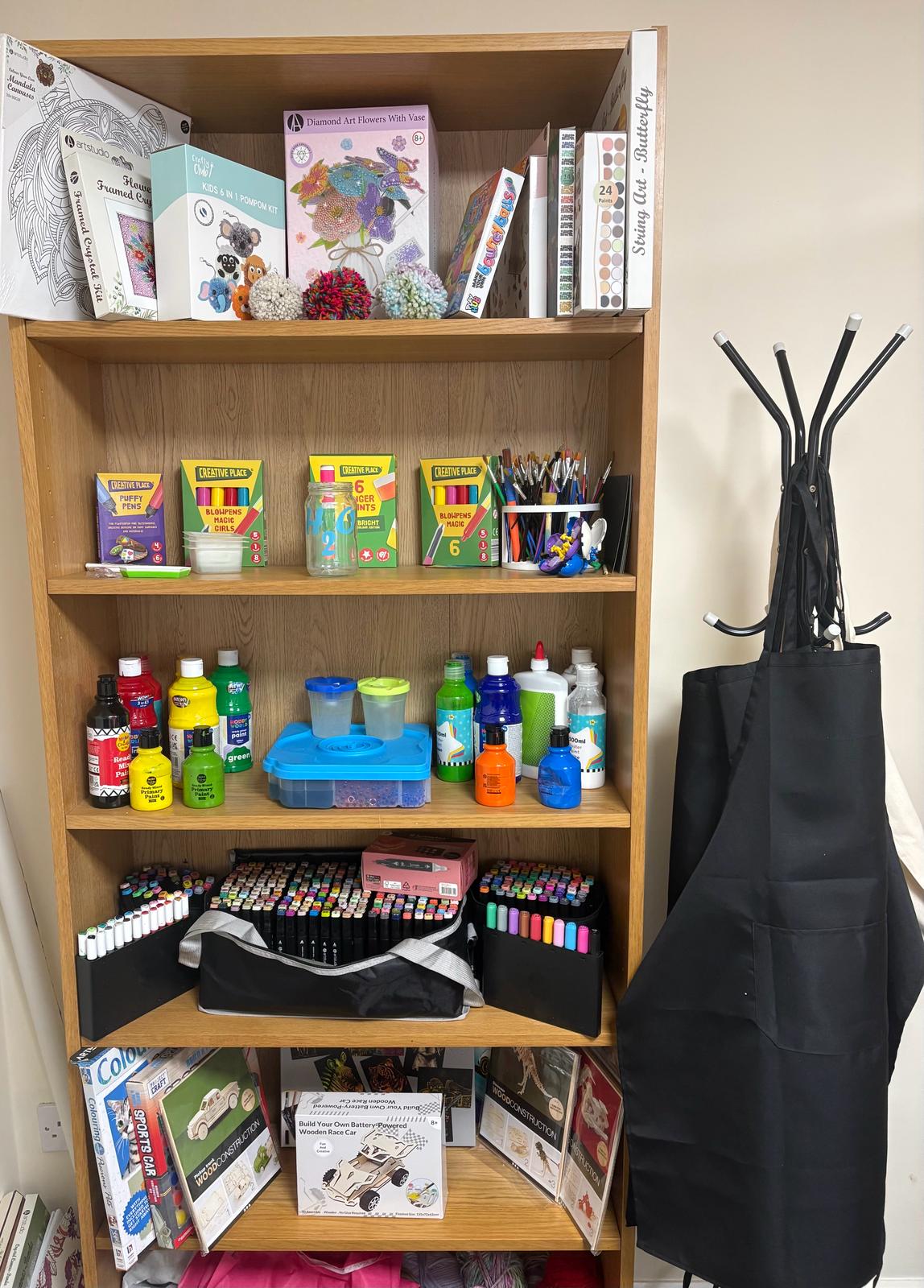 Wooden shelves stocked with colourful art supplies including paints, pens, craft kits and building sets
